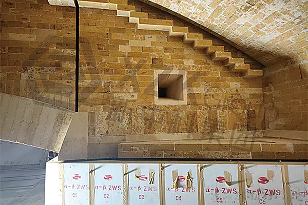 Stepped crown corner brickwork around a port opening, with AZS grades boxed and staged ready for installation.